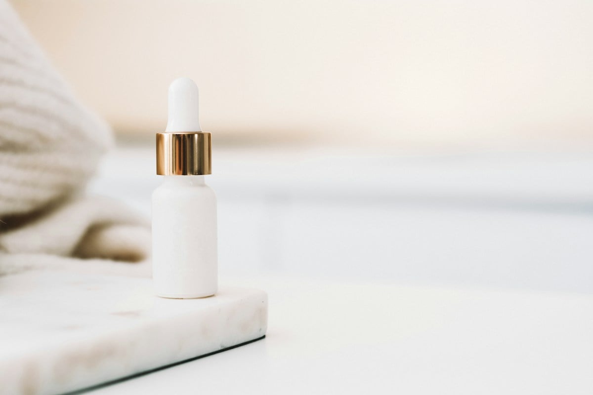 White skincare dropper bottle with gold collar on pale stone