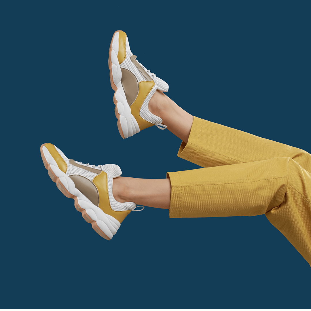 Yellow and white sneakers shown in on-foot lifestyle photography against a navy background