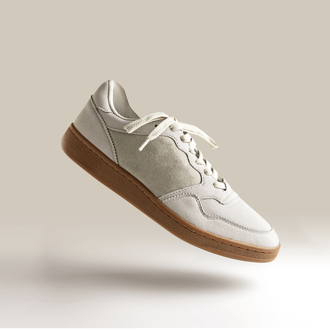 Single beige suede sneaker with a gum sole floating against a warm neutral background