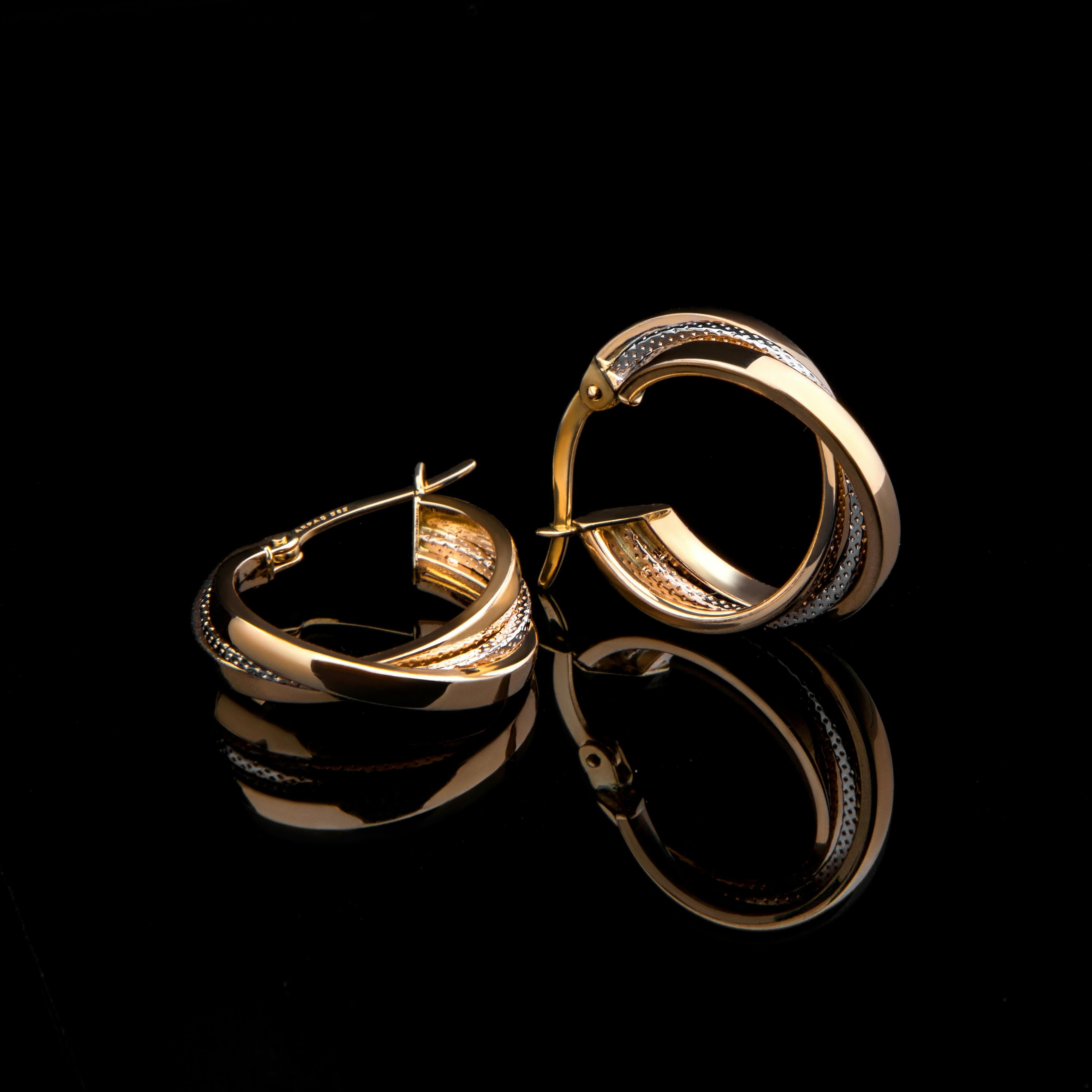 Gold hoop earrings on a glossy black surface with a clear mirrored reflection